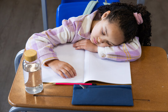 African American child sleeping head resting on notebook in class, blue pouch, in plaid jacket