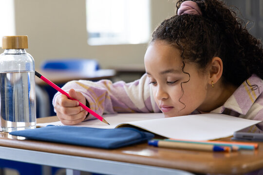 Youth African American girl writing in open notebook at classroom desk with pink pencil