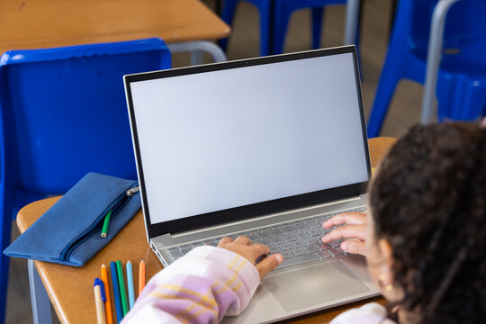Teenage African American female student typing on silver laptop in classroom in pastel plaid top