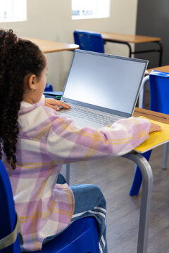 African American school child sitting at school desk using laptop with yellow folder and green pen