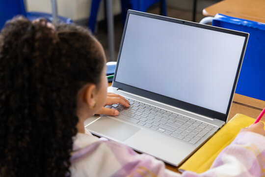 Youth African descent girl wearing hoodie sitting at school desk using laptop notes pen, copy space