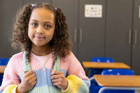 African American child standing in classroom wearing pastel sweater holding mint-green backpack