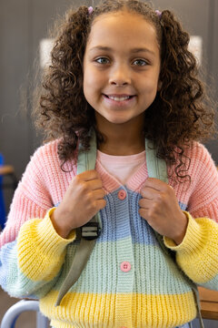 African American child standing at school, holding backpack straps and wearing pastel sweater