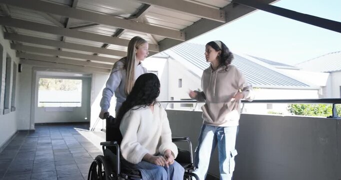 Female friends on covered walk, speaker gasping then stepping, urging wheelchair pushing by railing