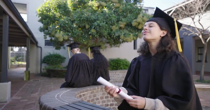 Diverse female grads in gown sitting on campus holding diploma savoring moment smiling, copy space