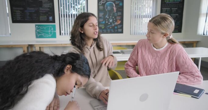 Three female students in class, center typing on white laptop explaining for class as left writing