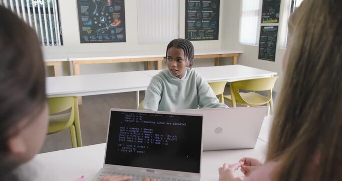 African peers typing in lab laptop showing code, leading center male in hoodie talking on project