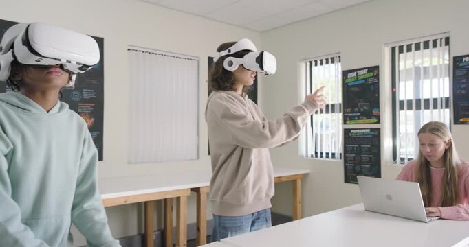 Student peers putting on white VR headsets, interacting with VR space in lab, laptop user watching