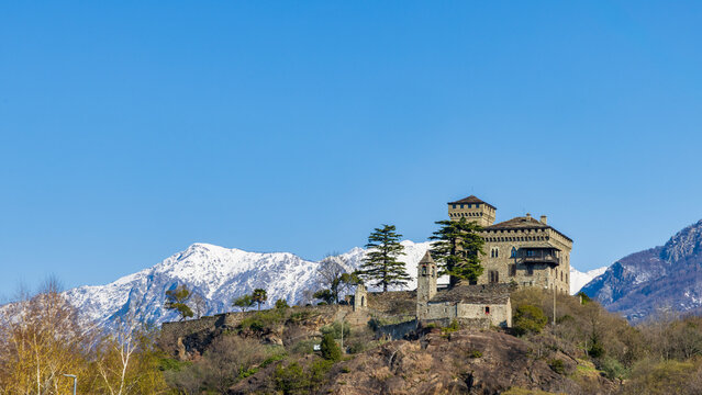 Medieval  castle Montestrutto  on a hill with snow‑capped Alps in Piedmont Italy under blue sky