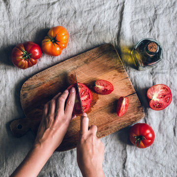 Hands slicing fresh tomatoes on a wooden cutting board, healthy meal preparation and home cooking concept with copy space