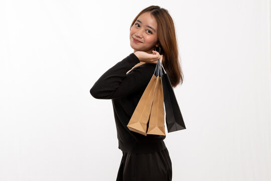 Stylish Asian shopper holding paper bags over shoulder enjoying retail sale white backdrop