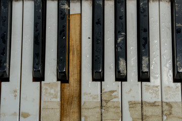 Damaged piano keyboard texture with ruined black and white keys. Top view background of a vintage musical instrument with weather-beaten surface details. © sandipruel