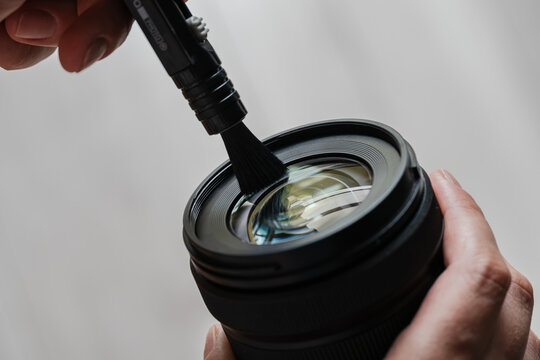 Photographer cleaning camera lens with brush for maintenance