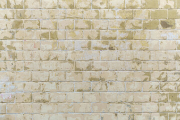 Fototapeta premium Brickwork backdrop with aged pale yellow tiles and cracked stucco fragments. Weathered architectural surface with repetitive rectangular patterns and rustic exterior texture.