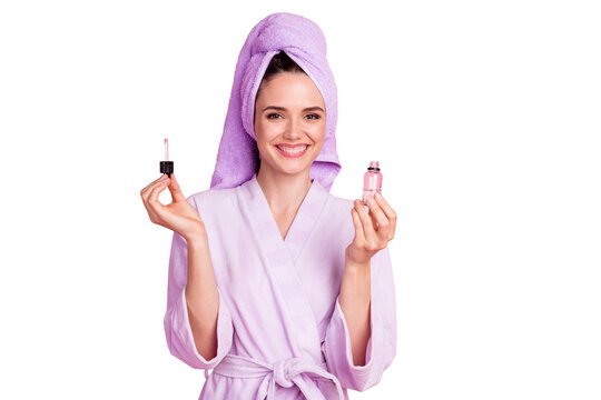 Portrait of pretty cheerful housewife wearing towel turban holding in hands facial natural oil bio serum isolated on pink pastel color background