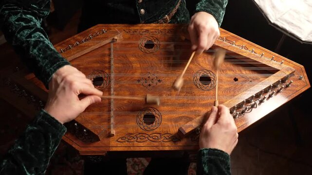 Musician playing hammered dulcimer with mallets, close-up of hands and strings.