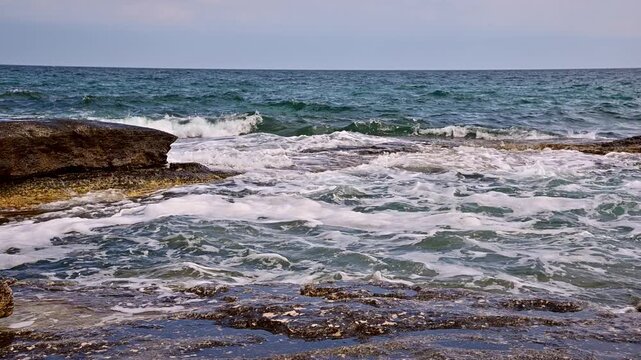 Waves crashing against rocky shore, slow-motion ocean scene with foam