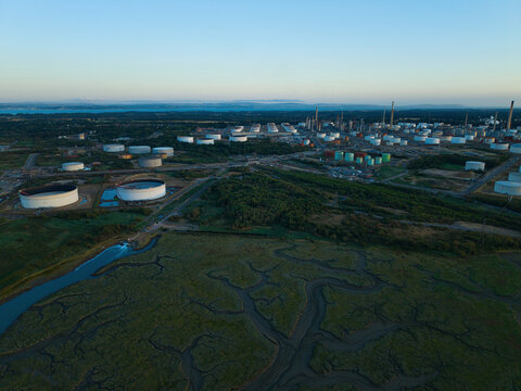 Aerial view of Fawley Refinery with its array of storage tanks, processing units, and chimneys situated along the coast near marshlands in Southampton, England, United Kingdom.