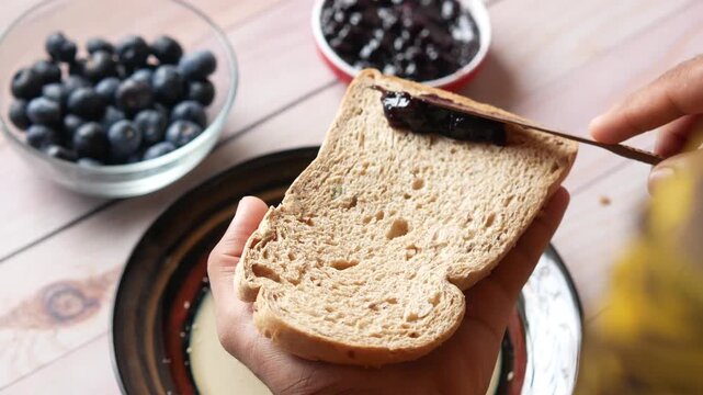 Spreading organic blueberry jam on fresh slice of whole grain bread for healthy breakfast