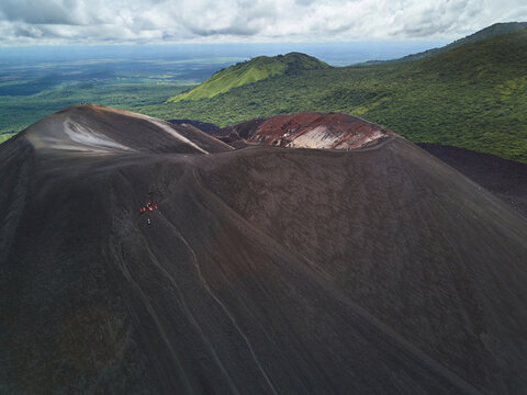 Aerial view of Cerro Negro volcano featuring dark volcanic slopes, a prominent crater, and small groups of hikers traversing the steep terrain in Leon, Leon, Nicaragua.