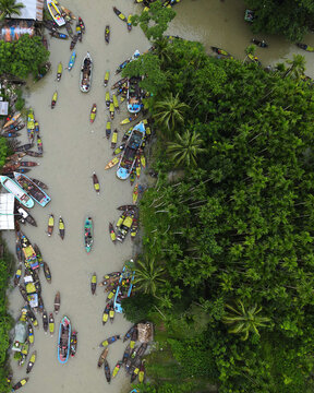 Aerial view of the Floating Guava Market with numerous wooden boats navigating the canal surrounded by lush green palm trees in Atghar Kuriana Union, Barisal Division, Bangladesh.