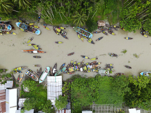 Aerial view of the Floating Guava Market with numerous small boats laden with produce navigating the canal surrounded by lush palm trees in Atghar Kuriana Union, Barisal Division, Bangladesh.