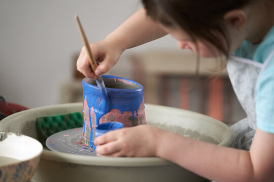 A primary school-aged girl painting a clay vase made on a pottery wheel. Close-up.  