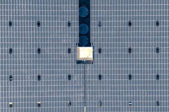 Aerial view of a large solar panel array with a geometric grid pattern and a central maintenance structure in Plano, Texas, United States.