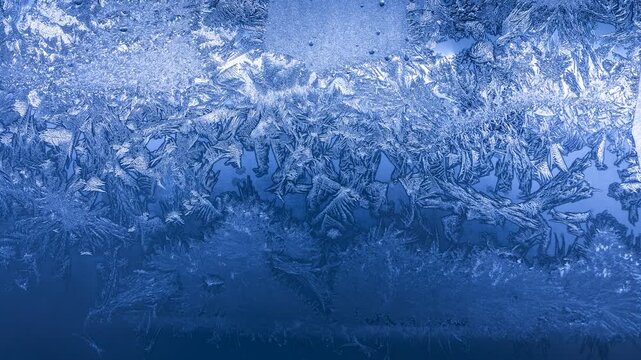 Frost crystal patterns forming intricate geometric shapes on glass in extreme winter cold
