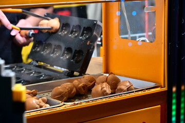 Fototapeta premium New Taipei City, Taiwan - Nov 16, 2025: Hands lift golden egg cakes from an iron mold in Banqiao District, steam rising beside a yellow street food stall.