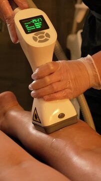 Vacuum roller massage. Lymphatic drainage and RF lifting stage. Dim atmospheric warm light. Masseuse massages a woman's leg with a device. self-care, care, weight loss. slow motion