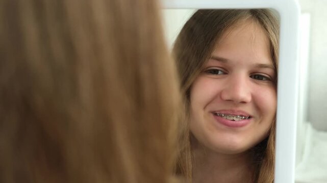 Smiling caucasian teenage girl with braces on her teeth looking at mirror. Happy teen with brackets looking at her reflection 