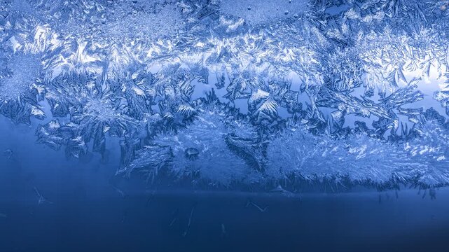 Frost crystal patterns forming intricate geometric shapes on glass in extreme winter cold
