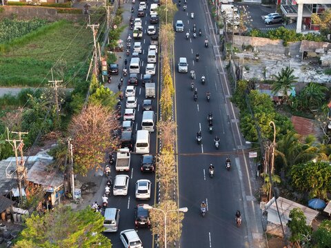 Aerial view of Simpang Sanur - Simpang Tohpati showing heavy traffic with cars and motorcycles on a busy road surrounded by trees and urban landscape in Denpasar Selatan, Bali, Indonesia.