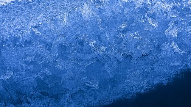 Frost crystal patterns forming intricate geometric shapes on glass in extreme winter cold
