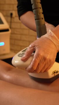 Vacuum roller massage. Anti-cellulite stage. Dim atmospheric warm light. Masseuse massages a woman's leg and thighs with a device. self-care, care, weight loss.