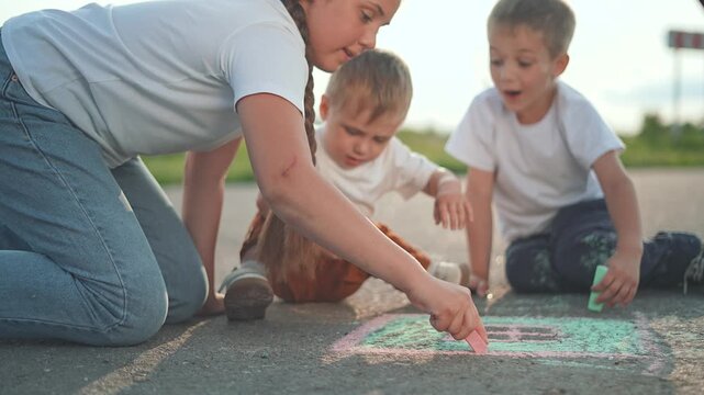Girl draws chalk path on sunny street. Kids follow her with more chalk drawings. Children collaborate with toddler watching. Chalk art spreads across street. Fun drawing time unites kids and children.