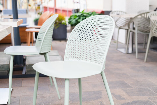 A light green chair is placed in an outdoor cafe space alongside another similar chair. The setting features potted plants and tables, creating a welcoming atmosphere