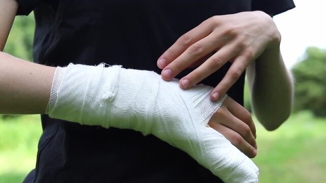 Injured person wearing a white bandage on their wrist while resting in a park during the day to help heal their arm from a recent accident or physical pain