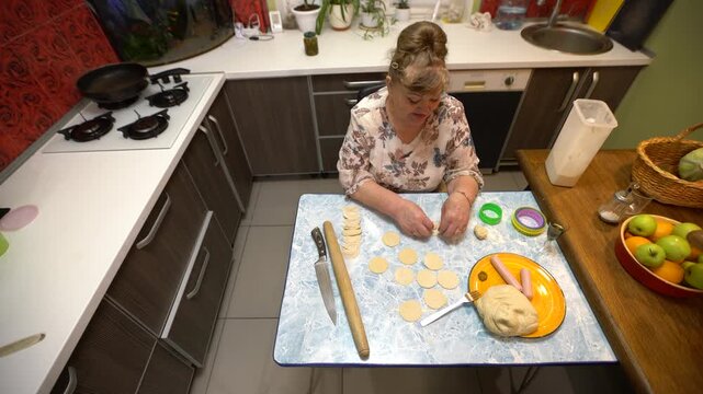 Woman shapes dough into dumpling circles.