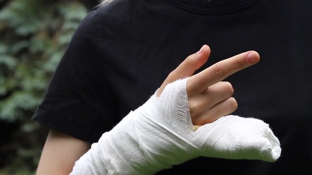 Young person wearing a black shirt shows an arm with a white medical bandage cast on the hand to help the bone heal during the day outside