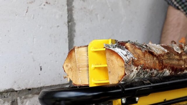 Person uses a yellow hand tool to split a piece of birch wood into smaller pieces for burning in a fireplace