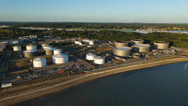 Aerial view of Hamble Oil Terminal featuring large fuel storage tanks along the coastline with industrial infrastructure and surrounding greenery in Hamble-le-Rice, England, United Kingdom.