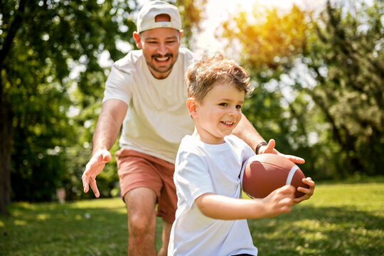 man and young boy playing american football on a court, teaching little player and spending time outdoors