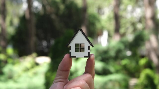 Hand holding small house model on green nature background. Insurance, real estate investment, mortgage and home loan concept
