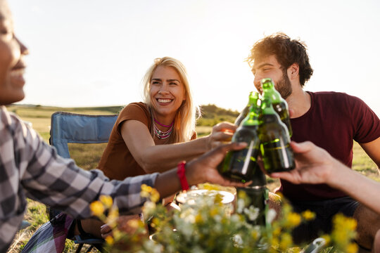 Friends Enjoying Drinks and Food While Sitting in a Grassy Field During Sunset