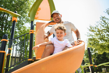 Fototapeta premium Happy boy kid on slider playground on summer season with his father