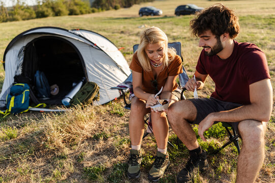Couple Enjoying Meal Together Outside Tent During Camping Trip in Green Field