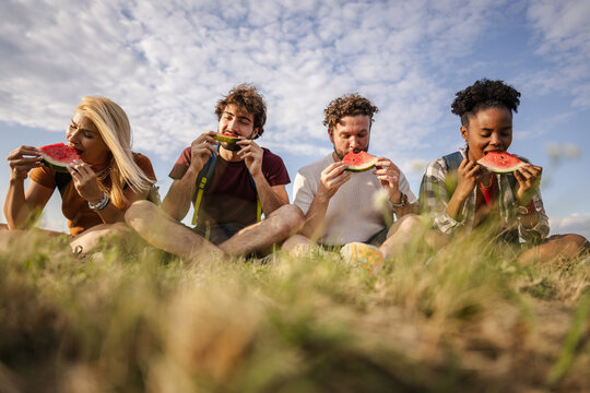 Friends Enjoying Watermelon While Sitting on Grass During Daytime in a Field