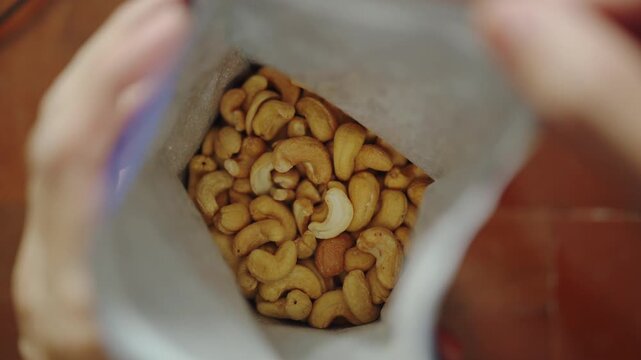 Macro Close Up View of Hand Opening Foil Bag Package of Roasted Salted Cashew Nuts Snack